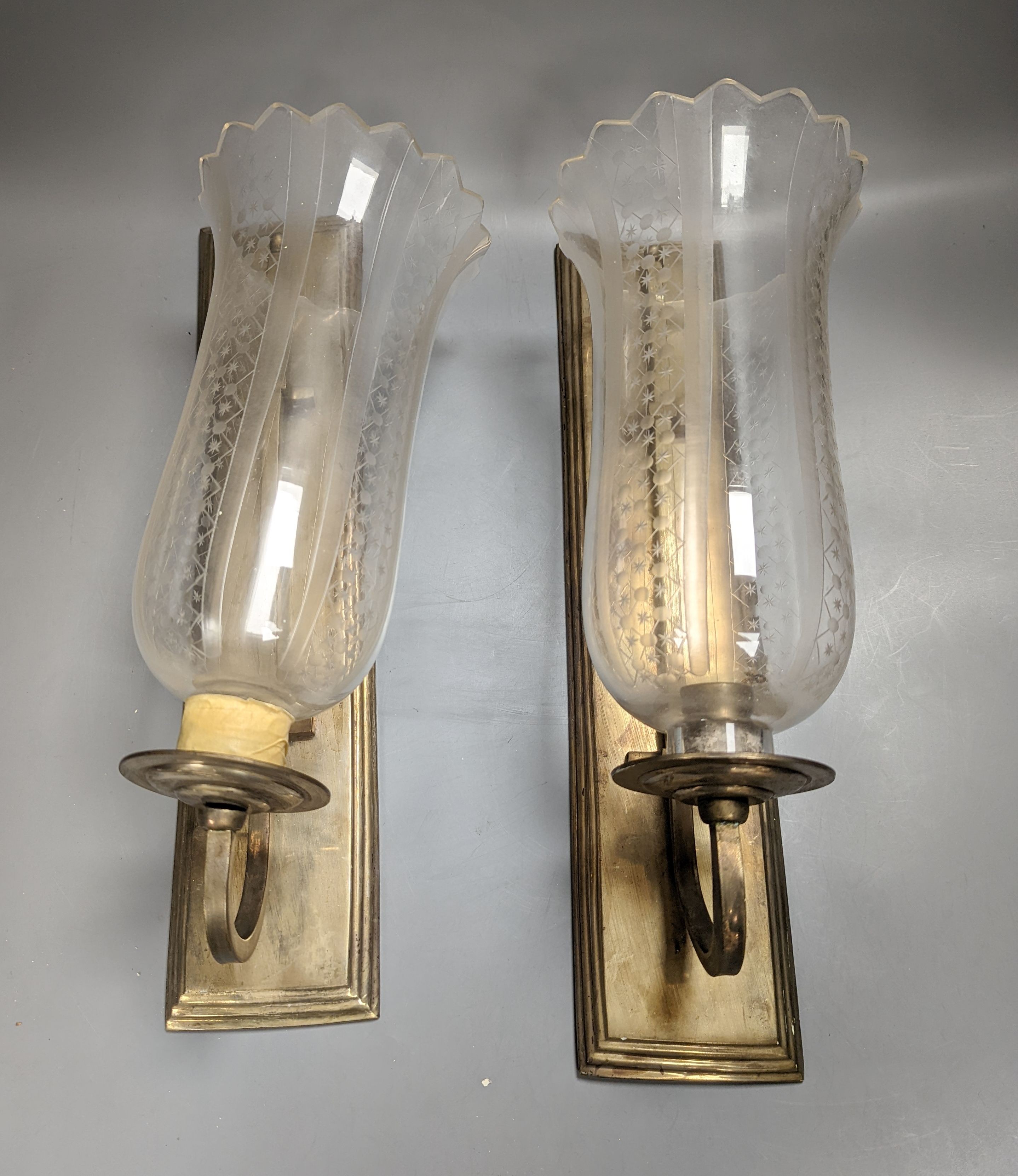 A pair of brass wall lights, with engraved glass storm shades, height 44cm